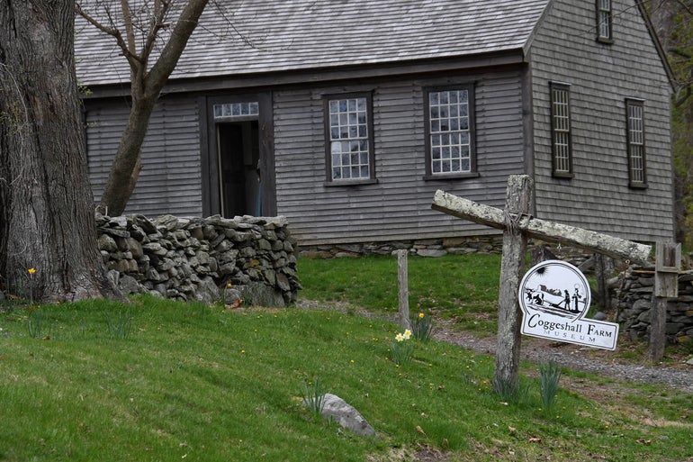 An old farmhouse sits behind a rock wall and grassy hill.