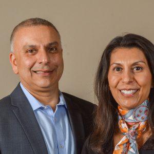 A man wearing a suit and a woman wearing a scarf smile at the camera.