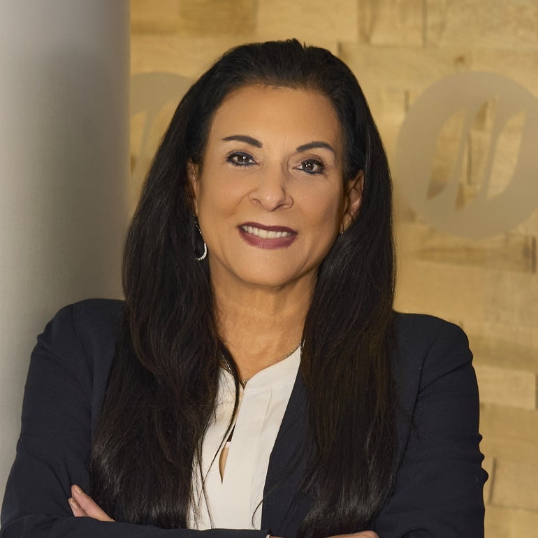A headshot of a woman with long black hair, a dark blue blazer, and a white top smiling for the camera