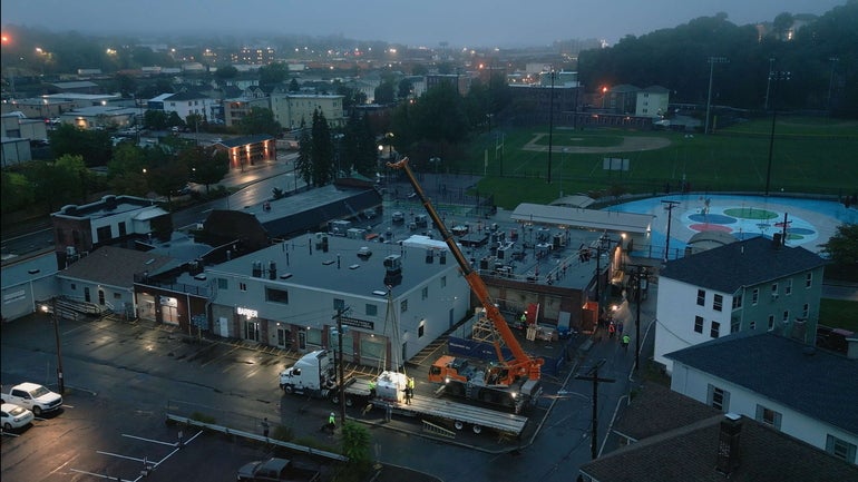 Aerial drone shot of a crane picking up a piece of large equipment with a foggy cityscape behind