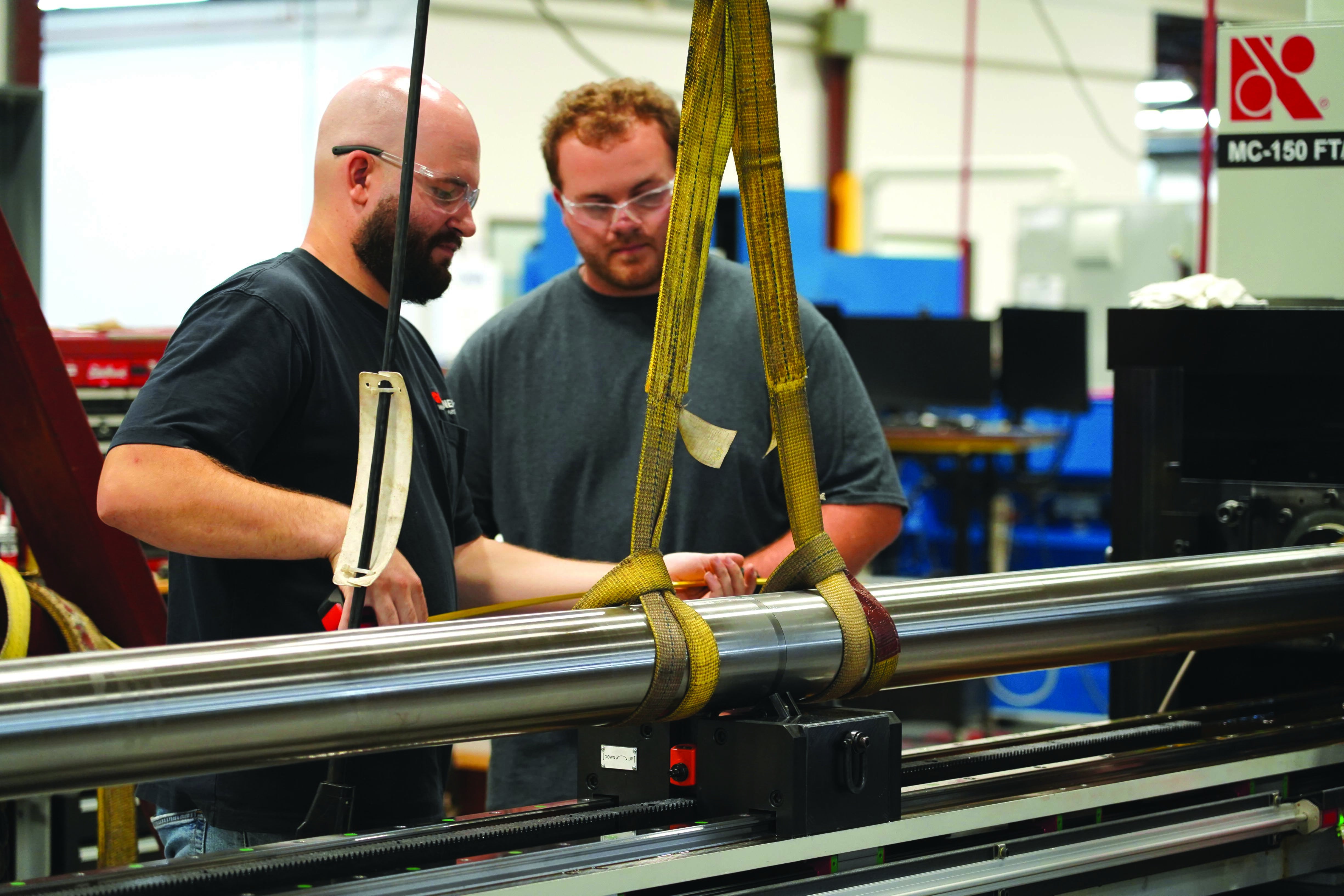 Two male manufacturing employees place a steel roll on a machine.