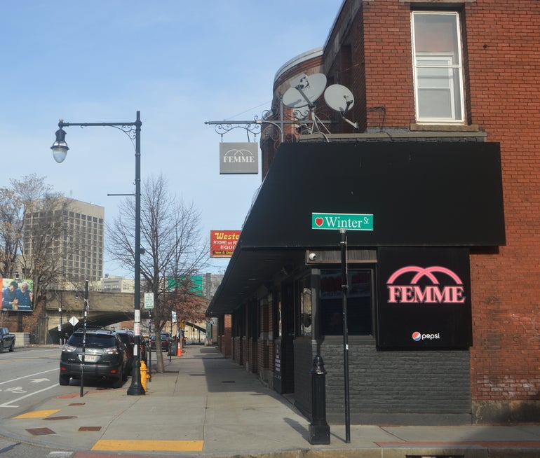 A bar on a urban street with a sign hanging out front which reads 