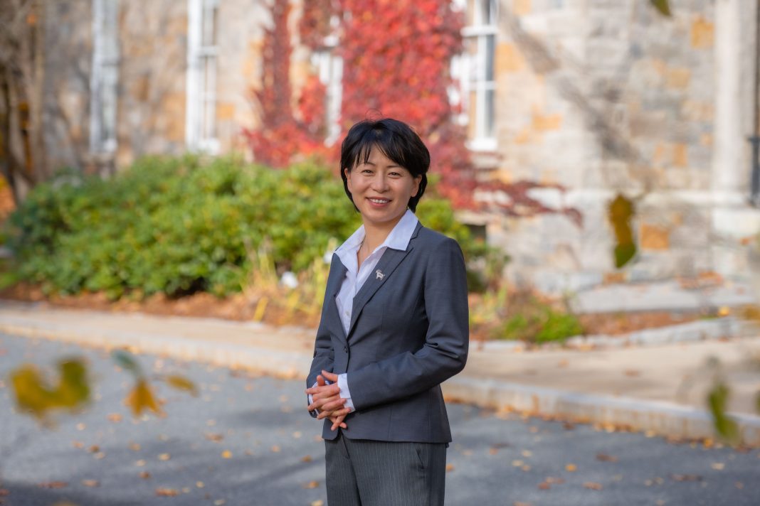 A woman with short, dark hair is wearing a blue shirt and blue suit