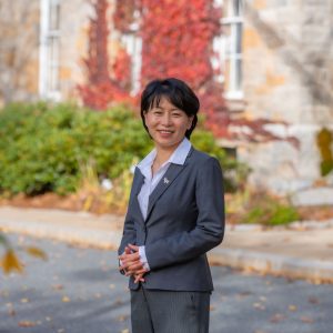 A woman with short, dark hair is wearing a blue shirt and blue suit