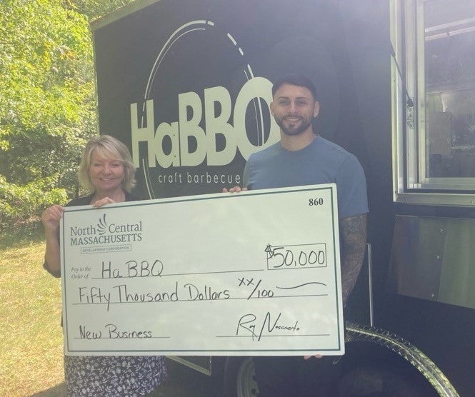 Two people stand with a giant check in front of a food truck