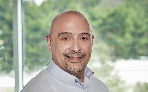Robert DaSilva smiling with trees seen through a window in the background
