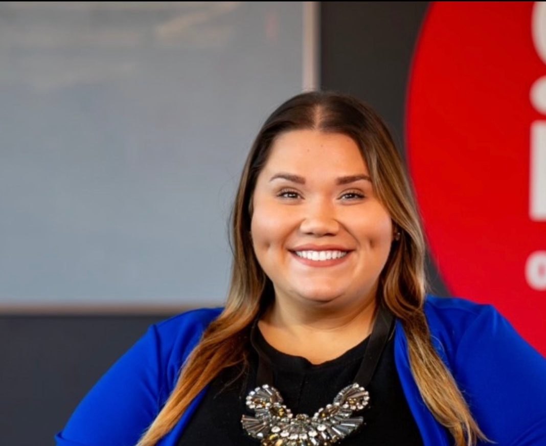 A woman with long hair wears a black shirt and a blue jacket