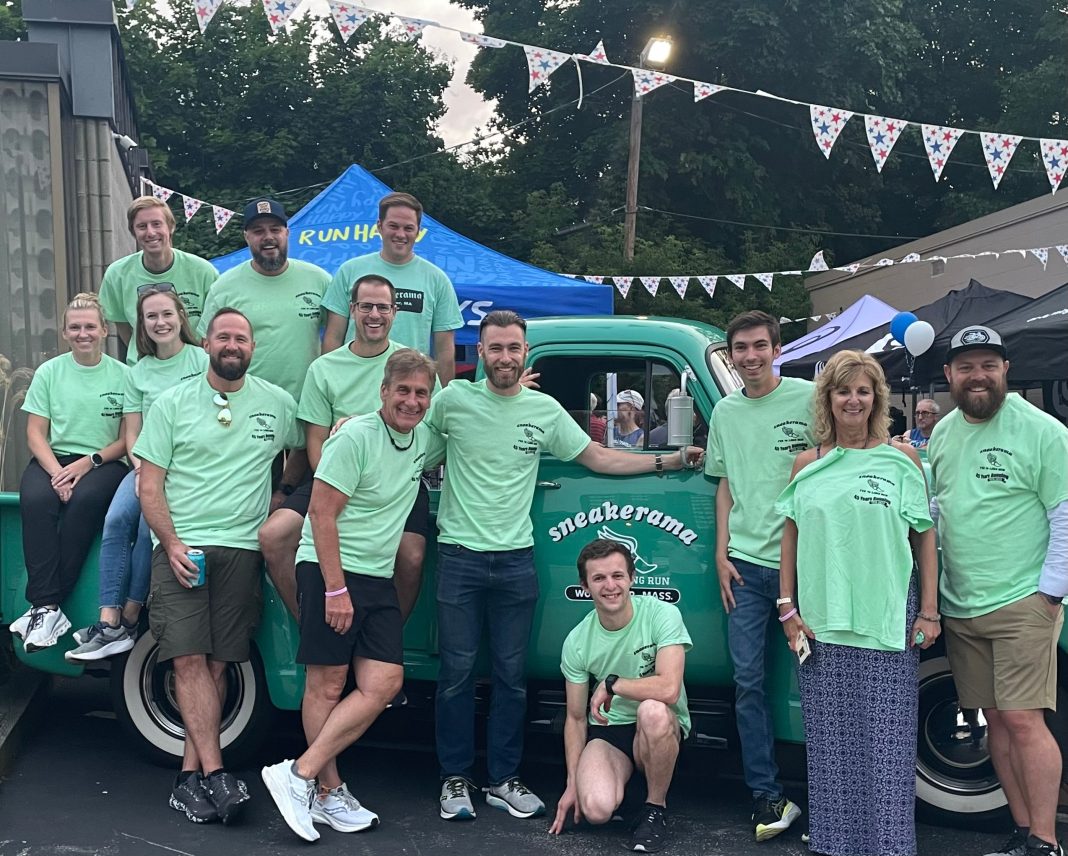 A group of men and women in light green shirts sitting on and standing in front of a green truck.