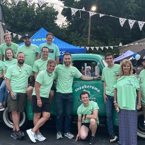 A group of men and women in light green shirts sitting on and standing in front of a green truck.