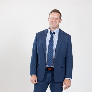 A man wears a blue suit with a blue-spotted tie.