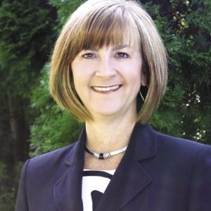 A woman with a light brown bangs and bob wears a dark blue blazer.