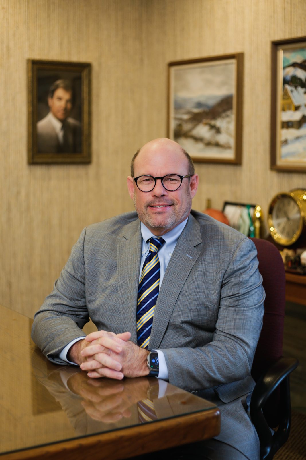 A man with glasses wearing a a gray suit sits at a table