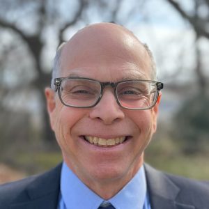A man with a suit and glasses smiles