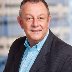 A man wearing a blue shirt and jacket smiles at the camera.