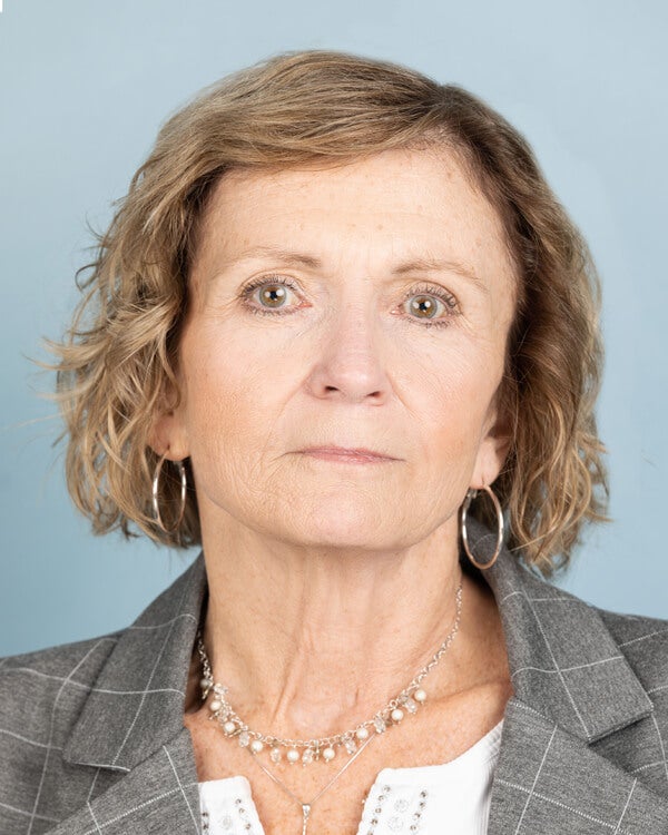 A woman with short, light hair is wearing a white shirt and gray jacket.