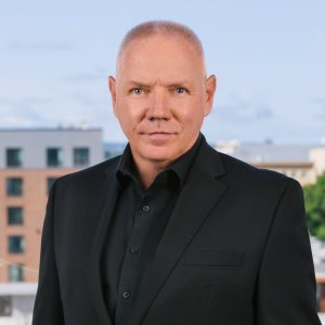 A man in a black suit with Worcester's skyline behind him