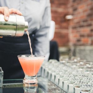 A bartender pours a pink drink from a shaker into a glass cup.