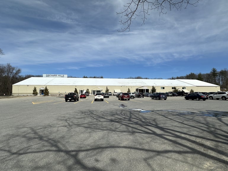 A large one-story, windowless building with a white roof and beige wall