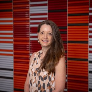 A woman with long brown hair stands in front of a colorful wall.