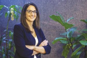 Woman in business attire and glasses smiles with arms crossed. 