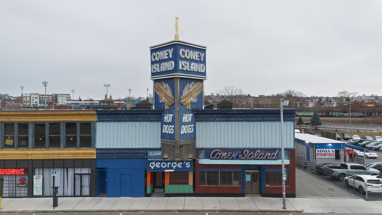 One grey and yellow building attached to a light and dark blue building with a large sign about it reading 