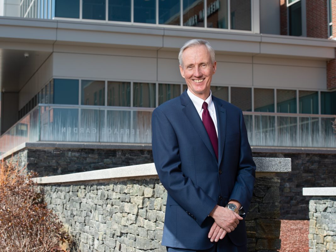 A man in a suit stands in front of a hospital