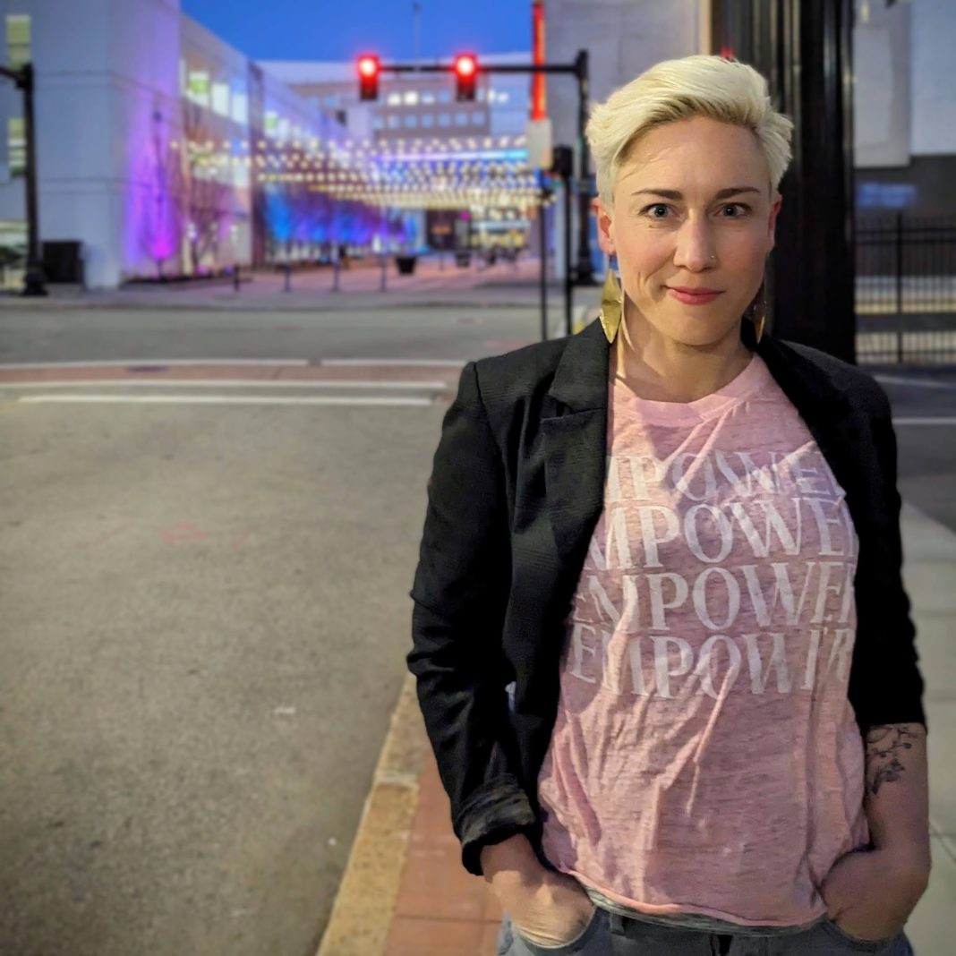 A woman wearing a black jacket and a pink shirt saying 