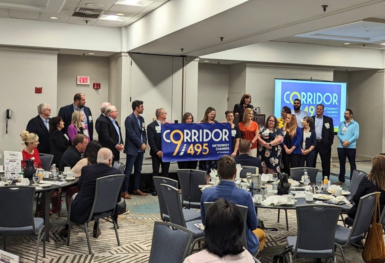 People sit at round tables and watch a group of people hold up a sign reading 