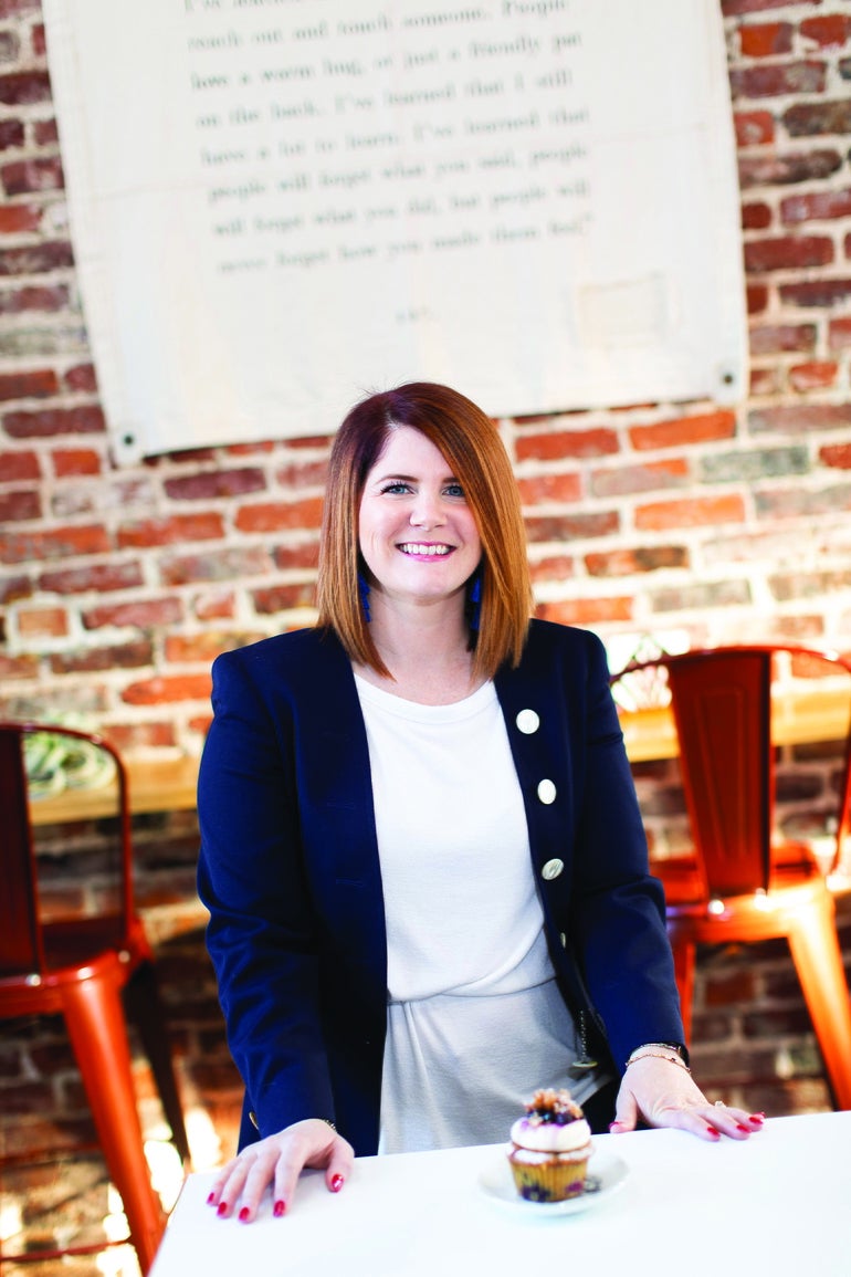 A woman stands behind a table with a cupcake on it
