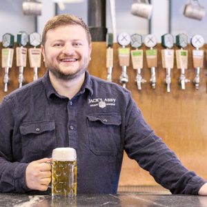 A man stands at a bar with a beer in his hand.
