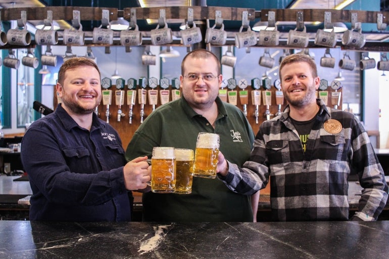 Three men holding beer steins while smiling