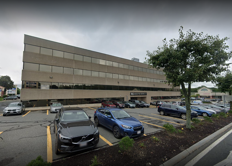 A large grey office building with a parking lot and cars in front.