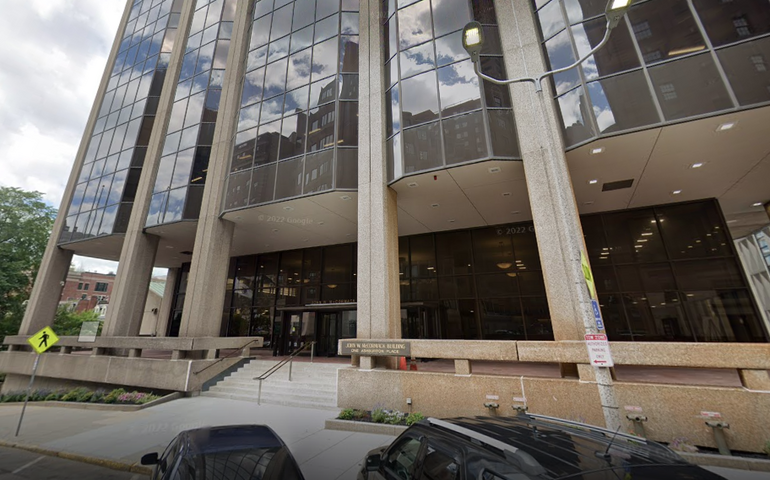 A large glass office building, with a small set of stairs leading to the door. Cars are parked in front.