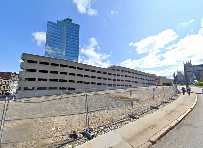 Empty fenced in lot sits in front of a parking garage