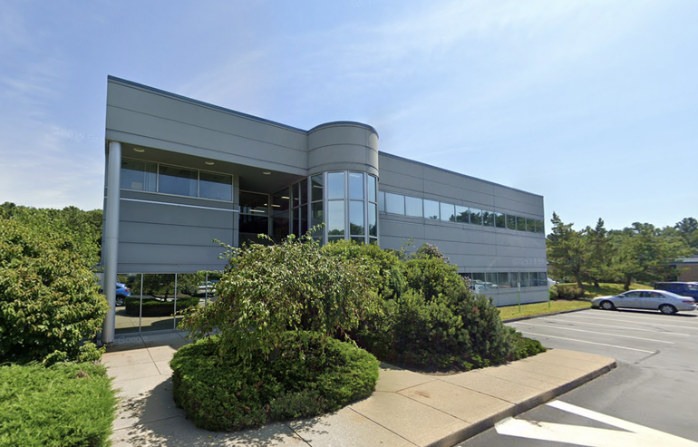 A building sits behind a parking lot with green shrubs in front.