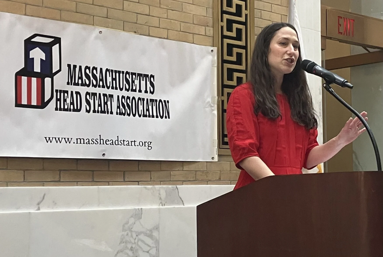 A person in a red dress speaks at a podium
