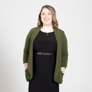 A woman with blonde hair stands with her hands in her cardigan pockets.