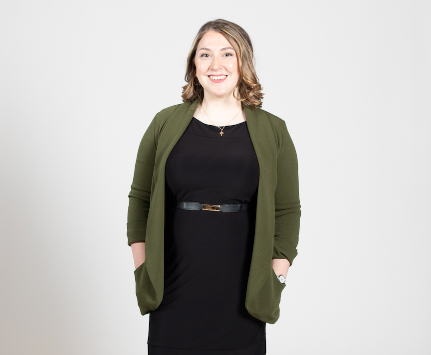 A woman with blonde hair stands with her hands in her cardigan pockets.