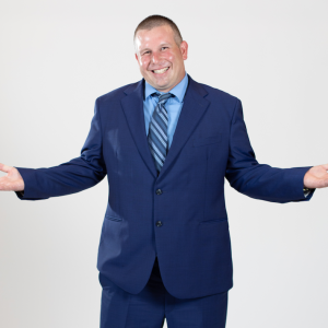 A man wearing a blue suit stands with his hands held out to his sides.