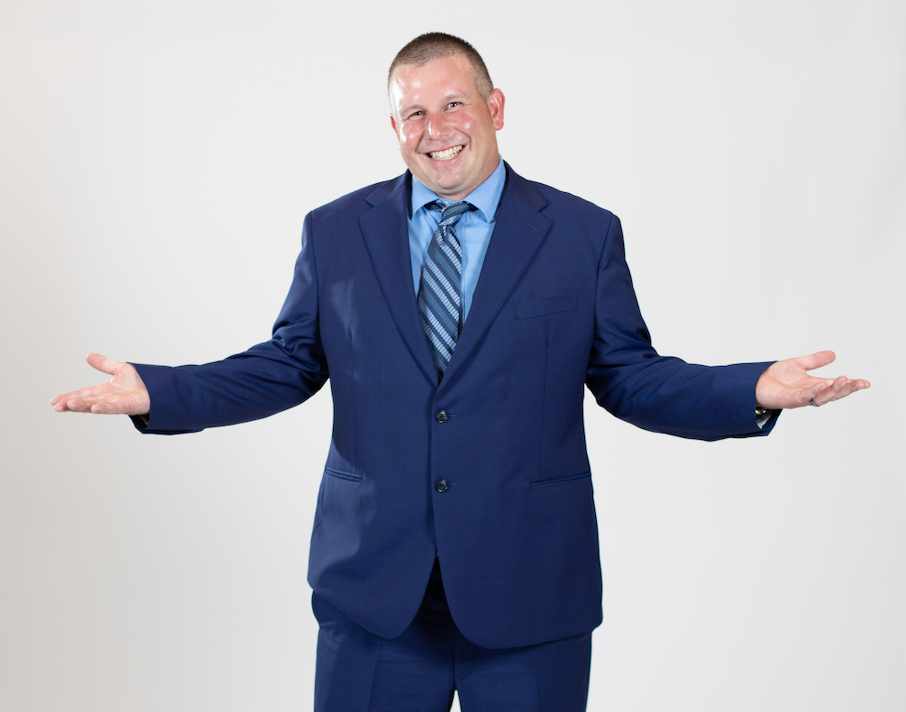 A man wearing a blue suit stands with his hands held out to his sides.