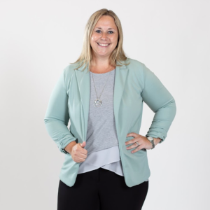 A woman with blonde hair wears a grey bouse and a pale blue blazer.