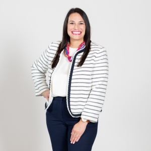 A woman with brown hair wears a white and black striped cardigan, a white blouse, and a jeans.