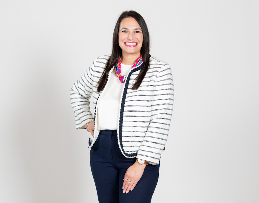 A woman with brown hair wears a white and black striped cardigan, a white blouse, and a jeans.