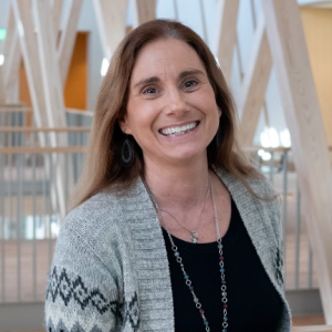 A woman with long light brown hair, a black shirt, and grey cardigan.
