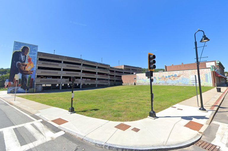 An empty lot with a parking garage featuring a mural and another building with a mural behind it.
