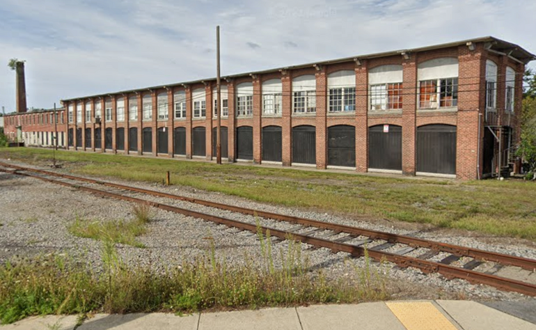 A mill building with train tracks and grass in front