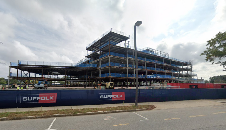 Scaffolding construction of a large hospital set back from a street with an overcast sky in the background