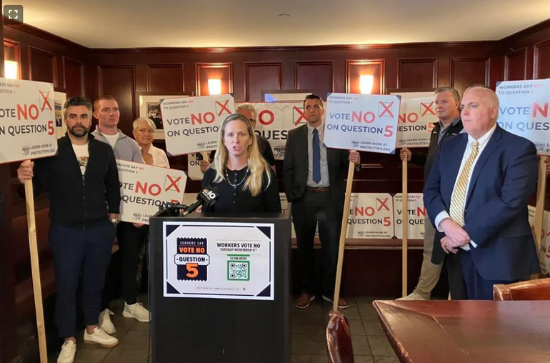 A group of people with political signs stand around a podium in an Irish bar