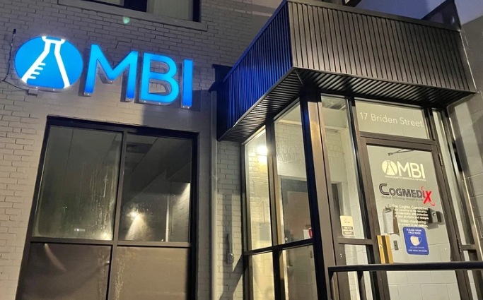 Outside of a white brick building with a lit up blue sign reading 