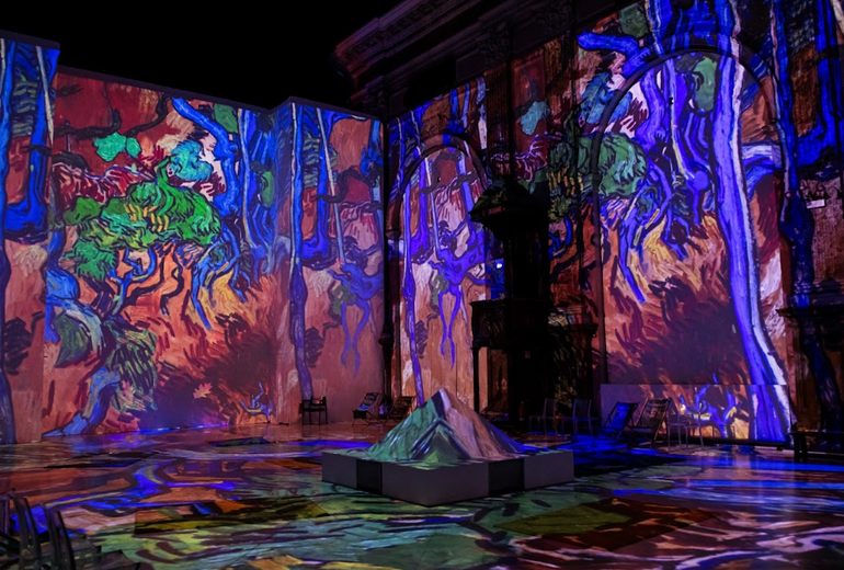A room with tall walls lit up with a projector showing a Van Gogh painting